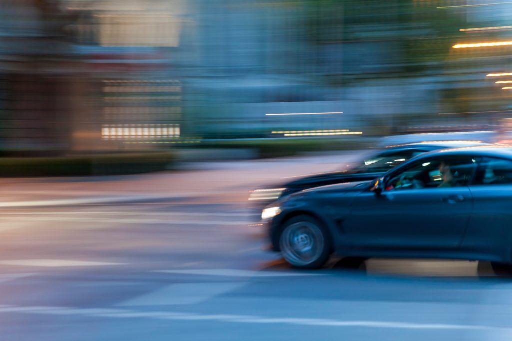 Imagen de un coche a gran velocidad en una calle de una ciudad urbana con poca luz natural.